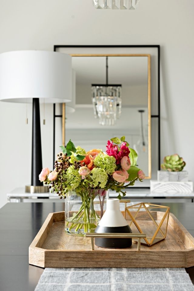 Flowers in a short vase on a wooden tray on top of a coffee table